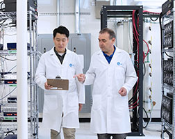 Image de deux personnes portant des blouses de laboratoire en train de marcher dans une salle de laboratoire.