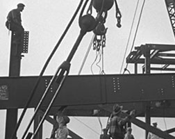 Black and white image of workers working on a steel railway bridge.