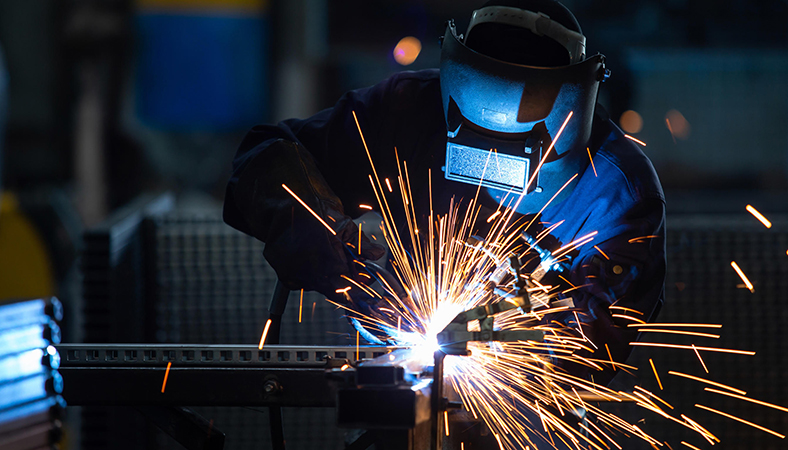 Featured Image. Person wearing welding mask and gloves, while welding metal.