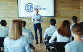 An instructor standing in front of the class, a screen with the CSA Group logo behind him