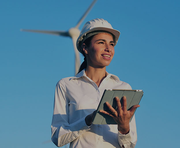 Une ingénieure portant un casque blanc et une tablette sur fond d’éoliennes